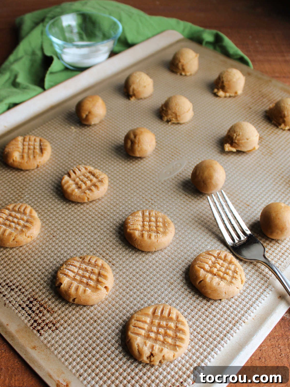 Tray of sourdough peanut butter cookie dough in various stages: some rolled into neat balls, others pressed with classic fork marks, showcasing preparation for baking.