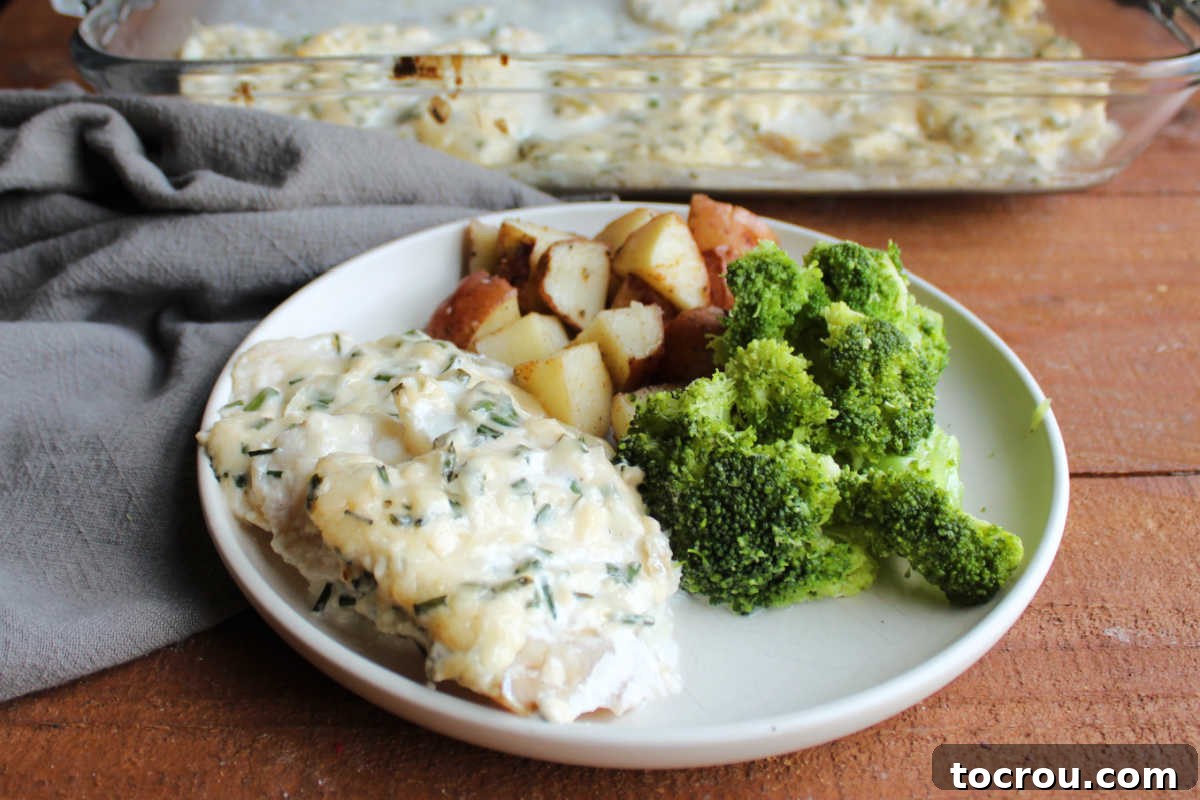 Parmesan baked cod topped with creamy sauce with specks of chives throughout served with broccoli and potatoes, ready to eat. A perfect healthy fish dinner.