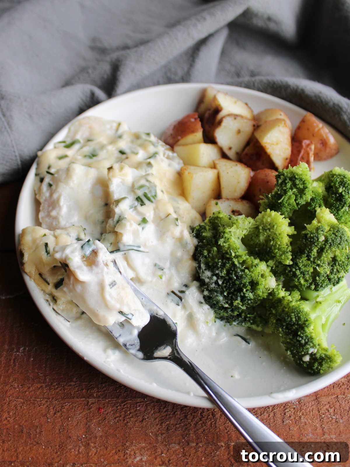 Bite of flaky cod topped with creamy parmesan sauce, ready to eat, showing the perfect texture of the fish.