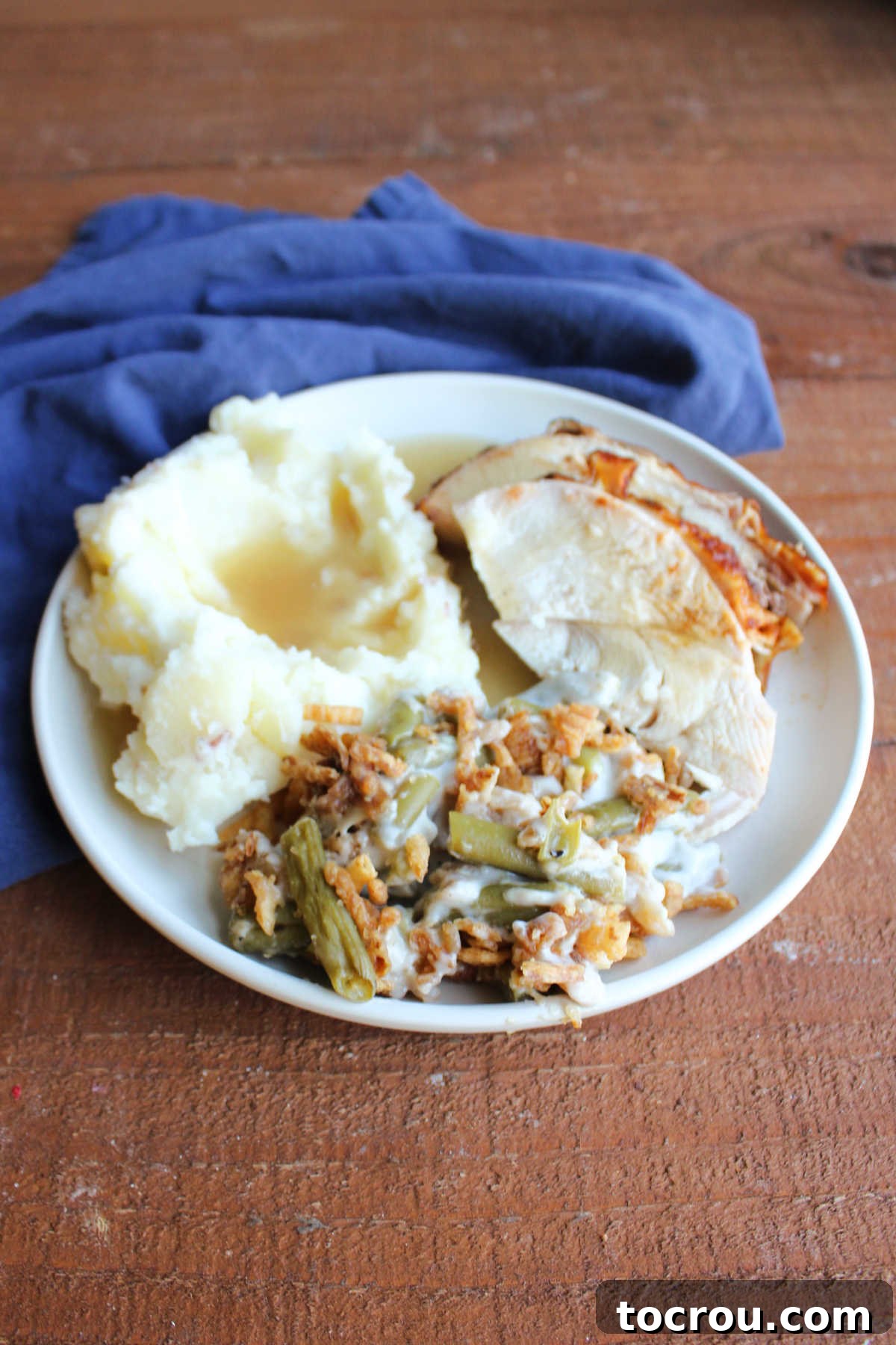 A close-up view of a dinner plate showcasing creamy classic green bean casserole, succulent sliced turkey, and fluffy mashed potatoes with savory gravy, emphasizing the dish's irresistible texture.
