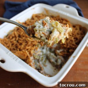 Serving spoon getting a scoop of classic green bean casserole with creamy mushroom soup and crispy fried onion topping from a warm baking dish.