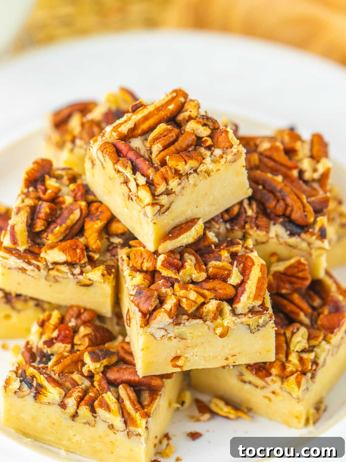 Close up of pecan pie fudge pieces showing light tan base with notes of vanilla and maple topped with crunchy pecans, ready to eat, highlighting the beautiful texture.