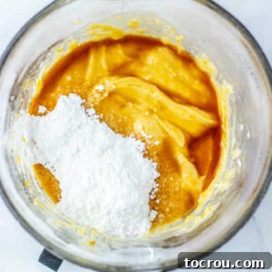 Adding the powdered sugar, vanilla extract, and maple extract to the bowl of melted white chips.