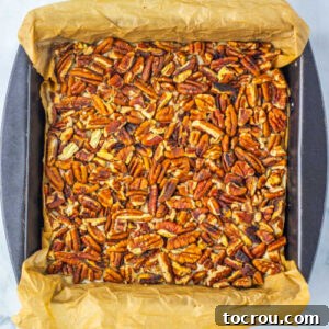 Pan of pecan pie fudge with toasted pecans on top, ready to be removed from the pan and cut into squares.