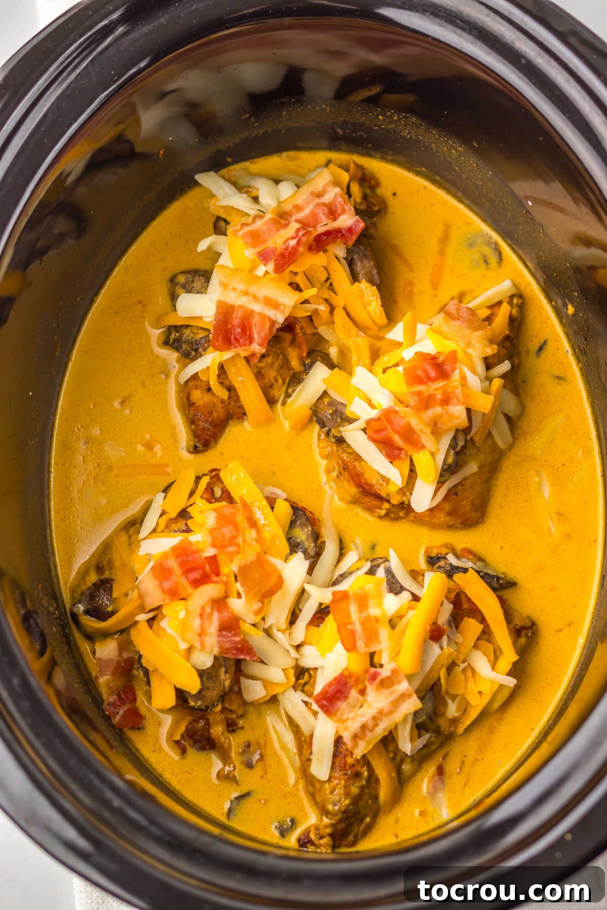Crockpot filled with chicken breasts cooked in a honey mustard sauce with mushrooms, bacon, and cheese, ready to be served.