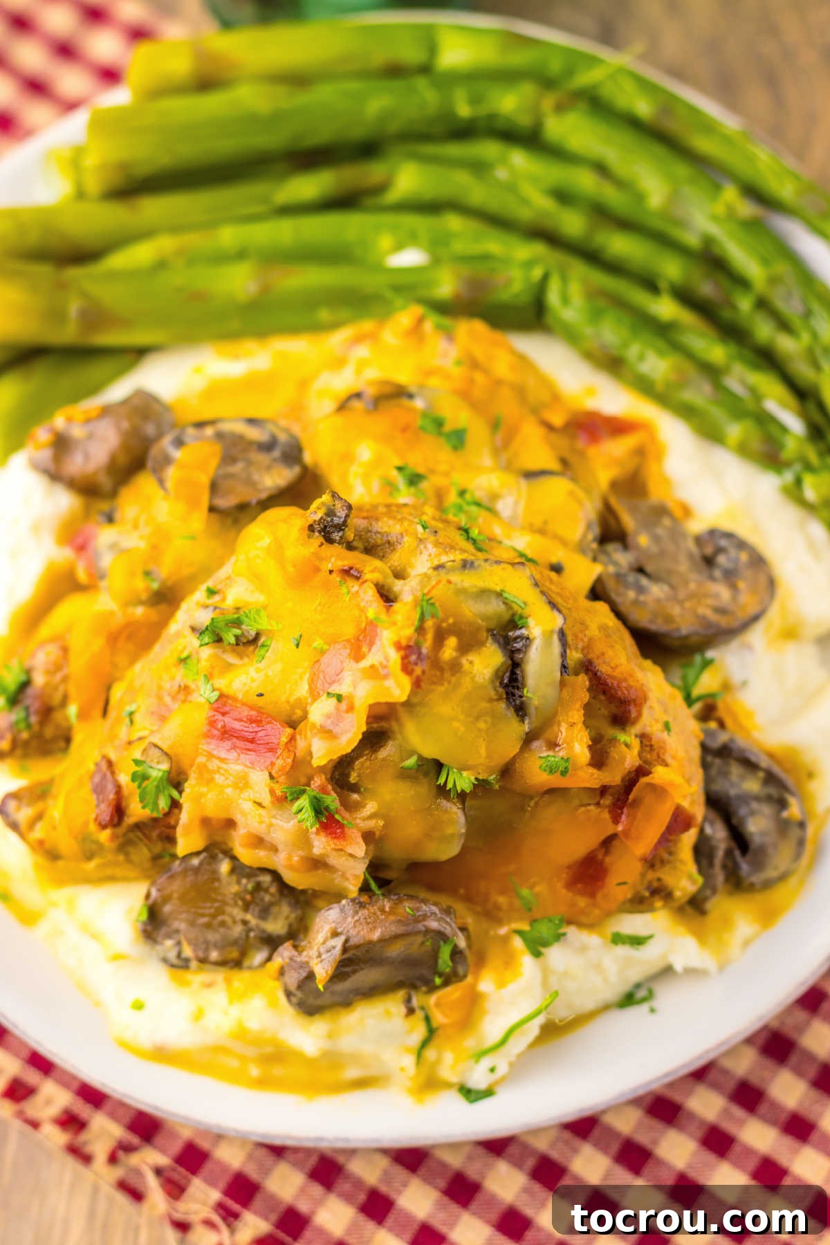 Pile of mashed potatoes topped with a chicken breast and creamy honey mustard sauce with mushrooms, bacon, and melted colby jack cheese, ready to eat.