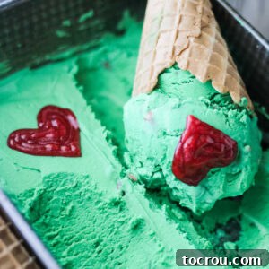 cone of green grinch ice cream with red icing hearts.