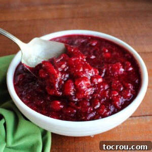 Antique berry spoon scooping out freshly made orange cranberry sauce with chunks of cranberries and a deep red color from a white serving bowl.