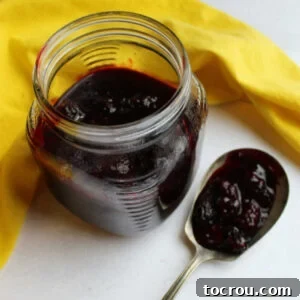 Jar of homemade blackberry sauce next to antique spoon filled with more blackberry sauce.