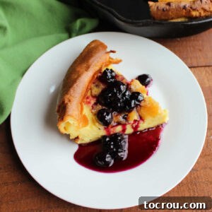 Slice of German pancake topped with homemade blueberry sauce, ready to eat.