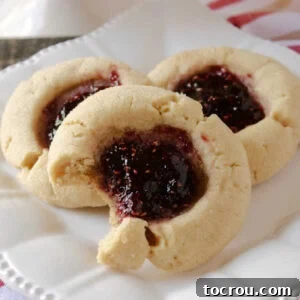 Plate with three peanut butter and jelly thumbprint cookies, one with a bite taken out.