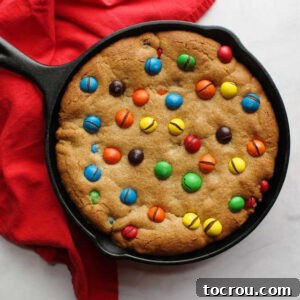 Cast iron skillet filled with soft peanut butter skillet cookie with peanut butter M&M's baked on top.