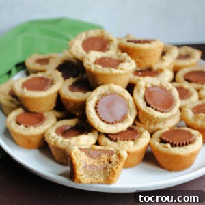 Pile of peanut butter cookies stuffed with Reese's peanut butter cups, one with a bite taken out showing center.
