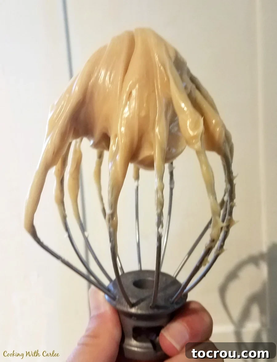 Caramel Frosting in Mixer Whisk attachment from a stand mixer filled with creamy caramel frosting.