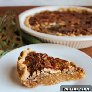 Slice of classic pecan pie with golden crust, gooey filling and lots of pecans on top.