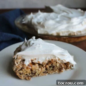 Slice of stupid pie on plate showing meringue type base with bits of cracker and pecans in it and fluffy white whipped topping on top. ready to eat.