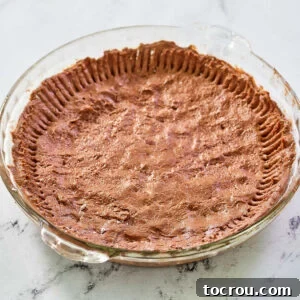 Chocolate pie crust pasty in glass pie dish, ready for filling.