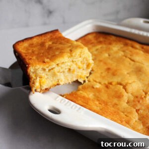 Feast Worthy Thanksgiving Sides 18 A spatula carefully lifting the first piece of golden-topped corn pudding casserole from its baking dish, revealing its soft, creamy interior.