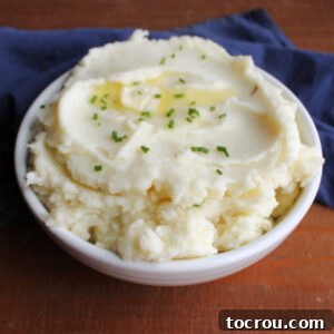 Feast Worthy Thanksgiving Sides 4 A serving bowl filled with creamy sour cream and chive mashed potatoes, generously topped with melted butter and sprinkled with fresh green chives, ready to be enjoyed.