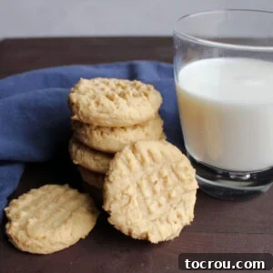 Heirloom Holiday Baking: From Grandma's Cookbook 16 Classic peanut butter cookies with characteristic fork hashmarks, neatly stacked beside a refreshing glass of milk, inviting a delightful snack.