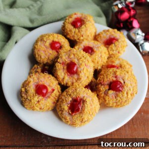 Heirloom Holiday Baking: From Grandma's Cookbook 20 A charming plate piled high with festive cherry winks cookies, featuring a delicate light pink cookie visible beneath a crunchy cornflake crumb exterior, highlighted by a bright red maraschino cherry in the center.