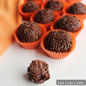 31 Sweet Homemade Treats 18 The soft, condensed milk chocolate center of a chocolate orange brigadeiro is revealed, with more sprinkle-coated truffles blurred in the background.