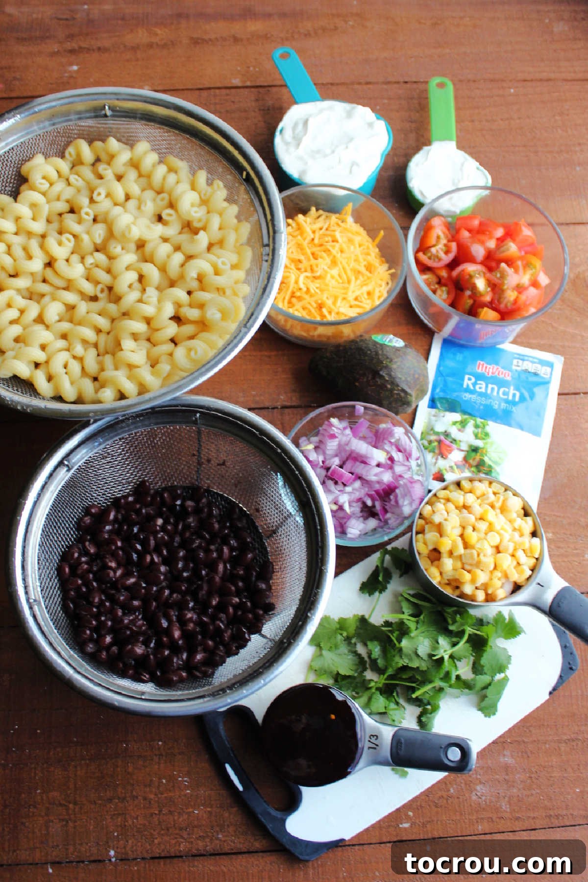 Fresh ingredients for BBQ Ranch Pasta Salad preparation Ingredients including cooked pasta, cheese, sour cream, ranch seasoning, corn, black beans, red onion, bbq sauce and cilantro ready to be made into bbq ranch macaroni salad.