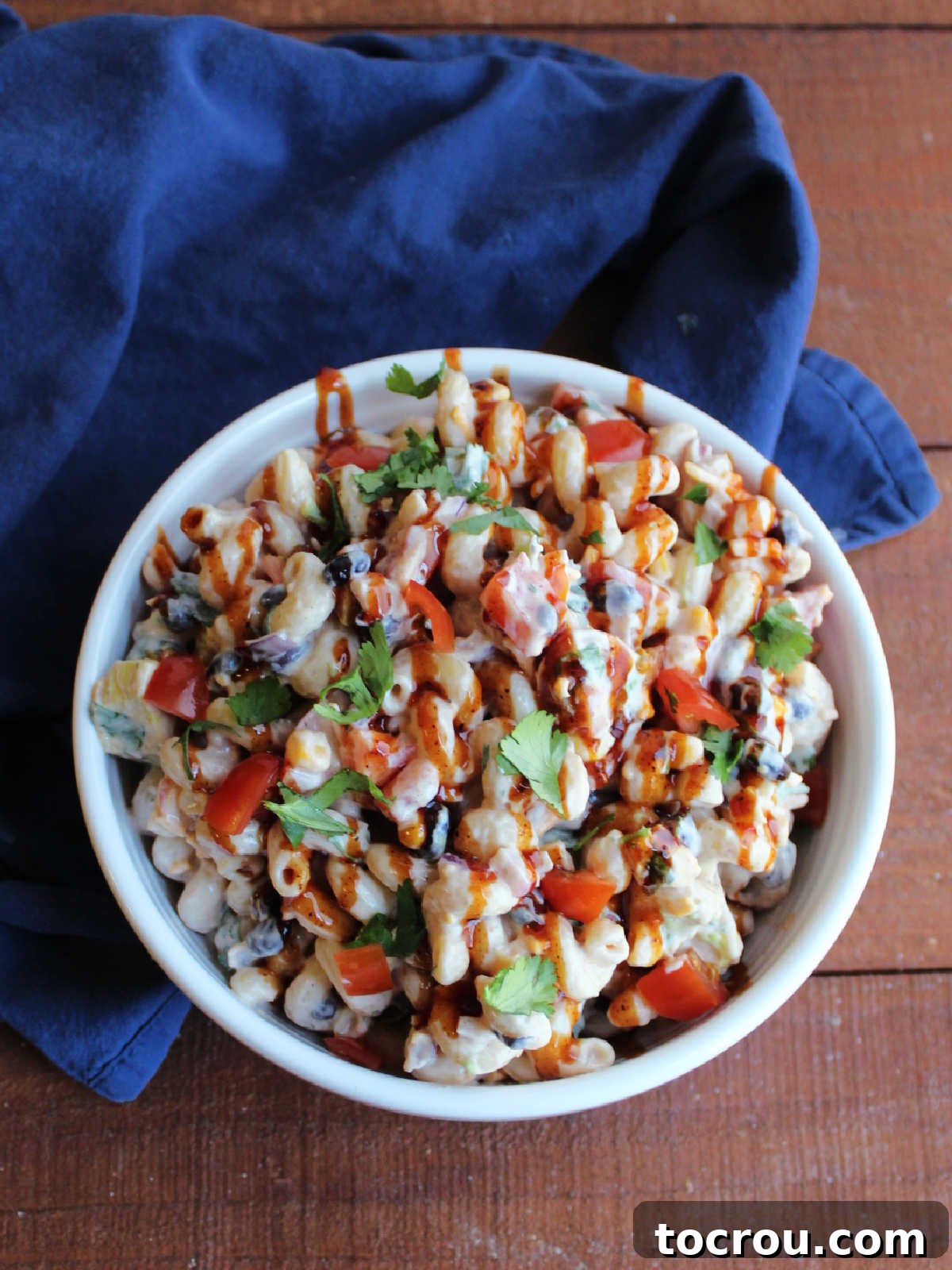 Garnished BBQ Ranch Pasta Salad ready to serve Serving bowl of bbq ranch pasta salad topped with fresh diced tomato, cilantro and a drizzle of bbq sauce.