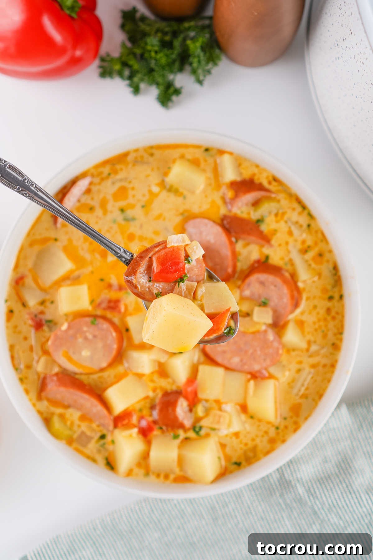 Bite of creamy potato soup with andouille sausage on spoon. 