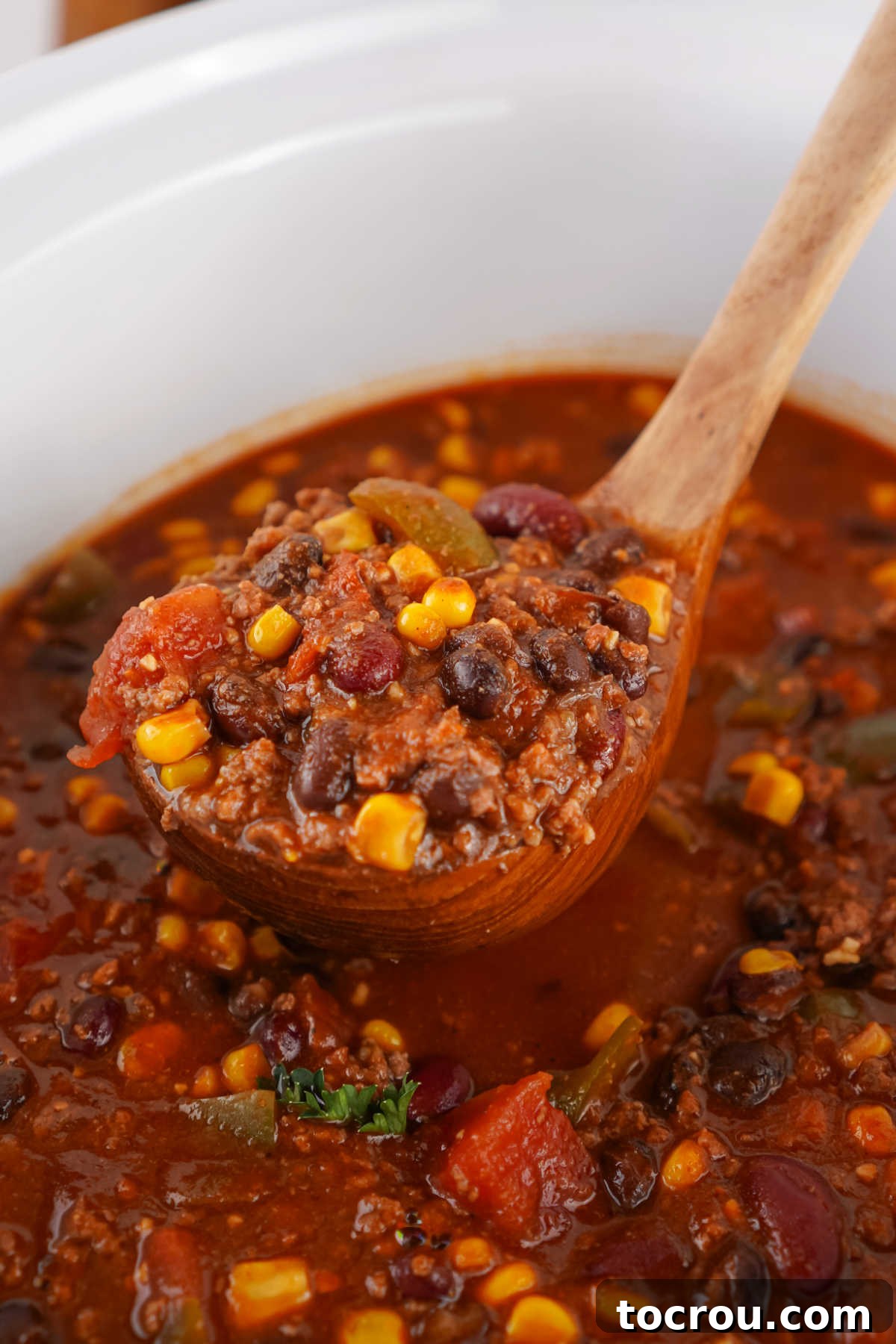 A ladle serving a generous helping of chunky Cowboy Soup from the slow cooker, highlighting its rich texture and plentiful ingredients.