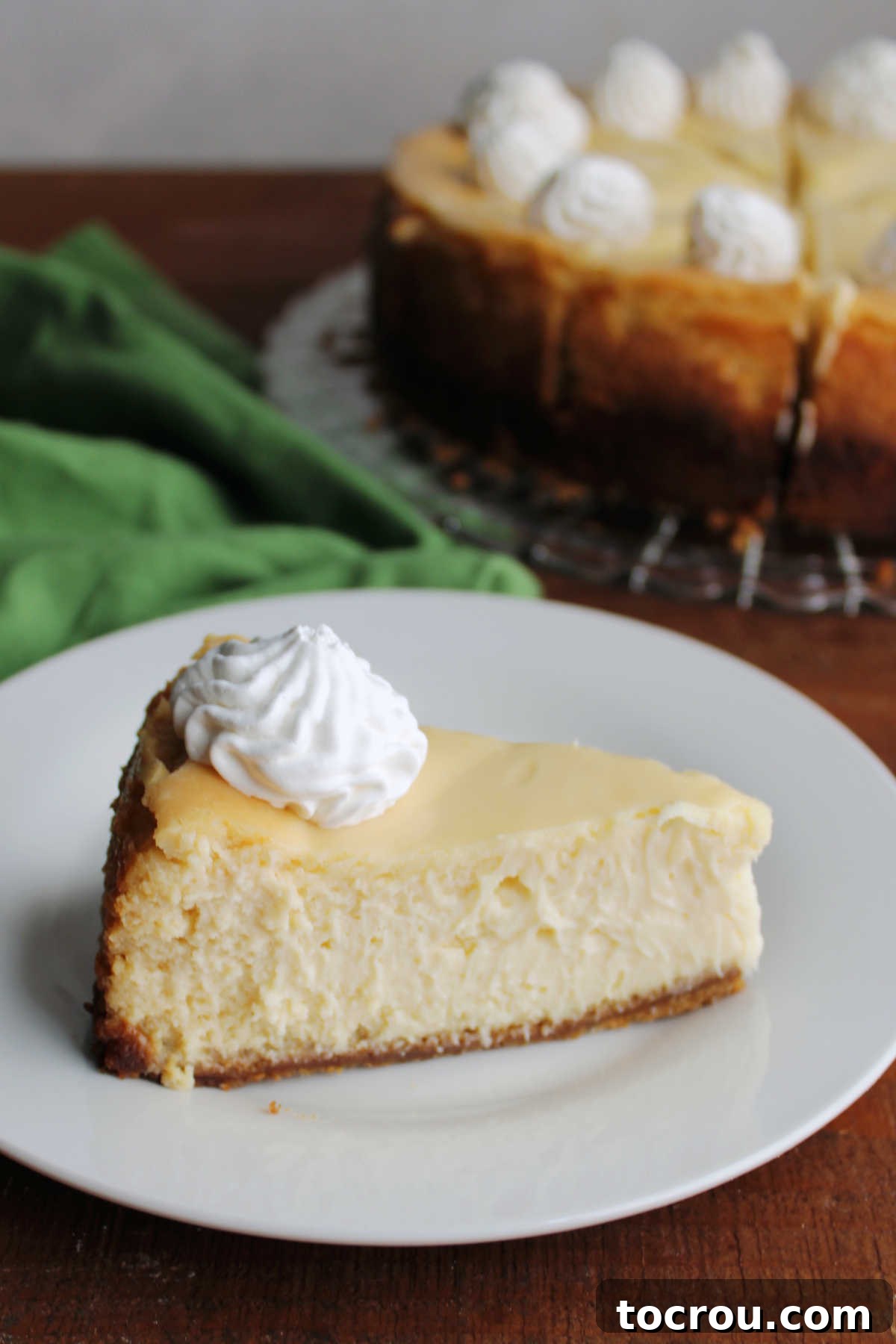 Key Lime Cheesecake with Whipped Cream A perfect slice of creamy Key Lime Cheesecake, adorned with a swirl of whipped cream, sits invitingly on a white plate, ready for dessert.