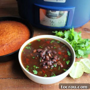 Bowl of black bean soup next to a skillet of cornbread, lime halves, and fresh cilantro.