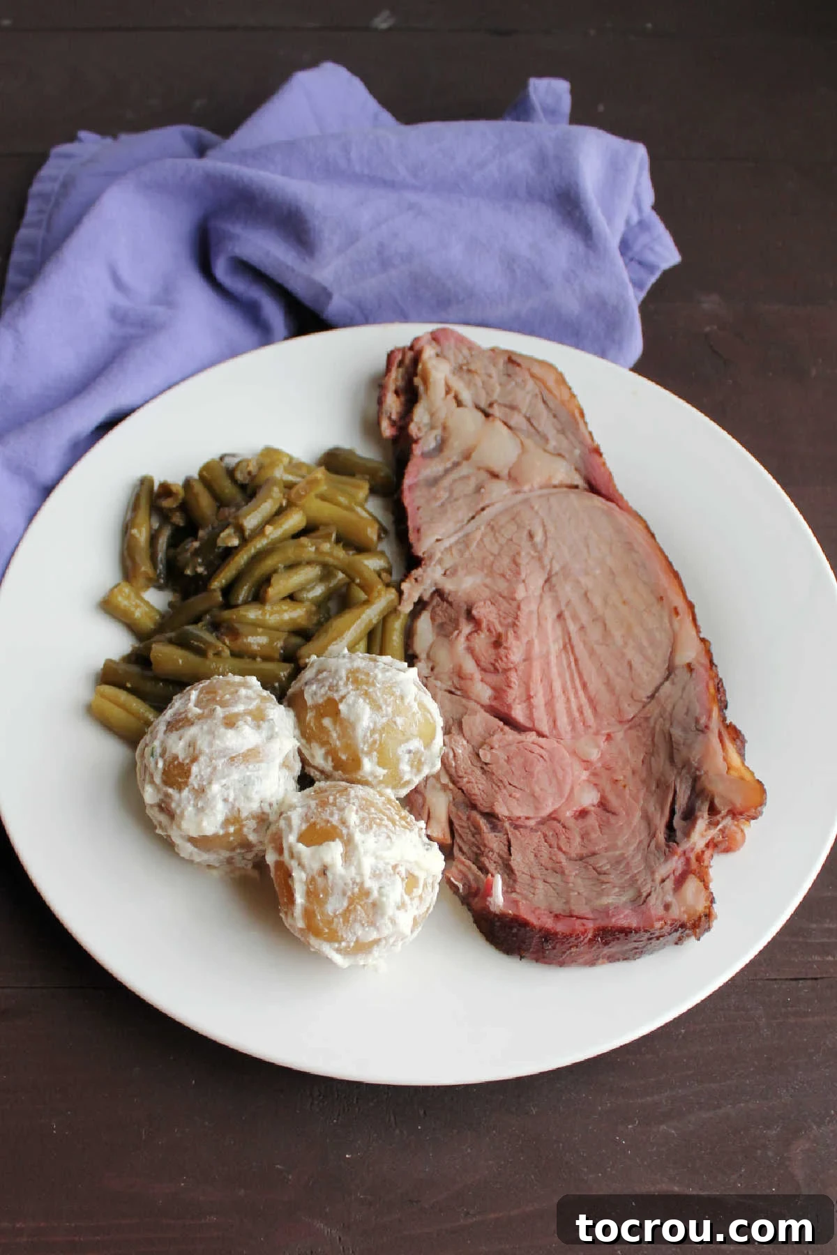 Slice of prime rib, smothered green beans and sour cream and chive coated new potatoes on plate ready to eat.