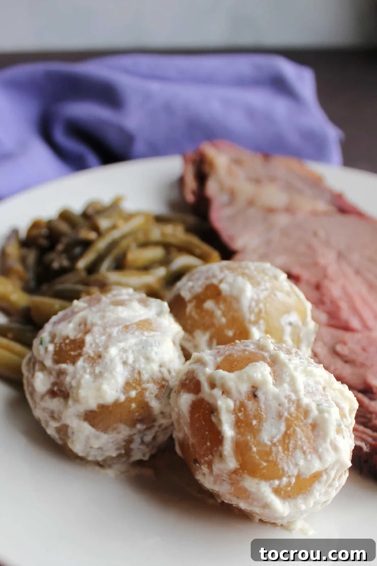 Close up of sour cream and chive potatoes on plate with green beans and beef.