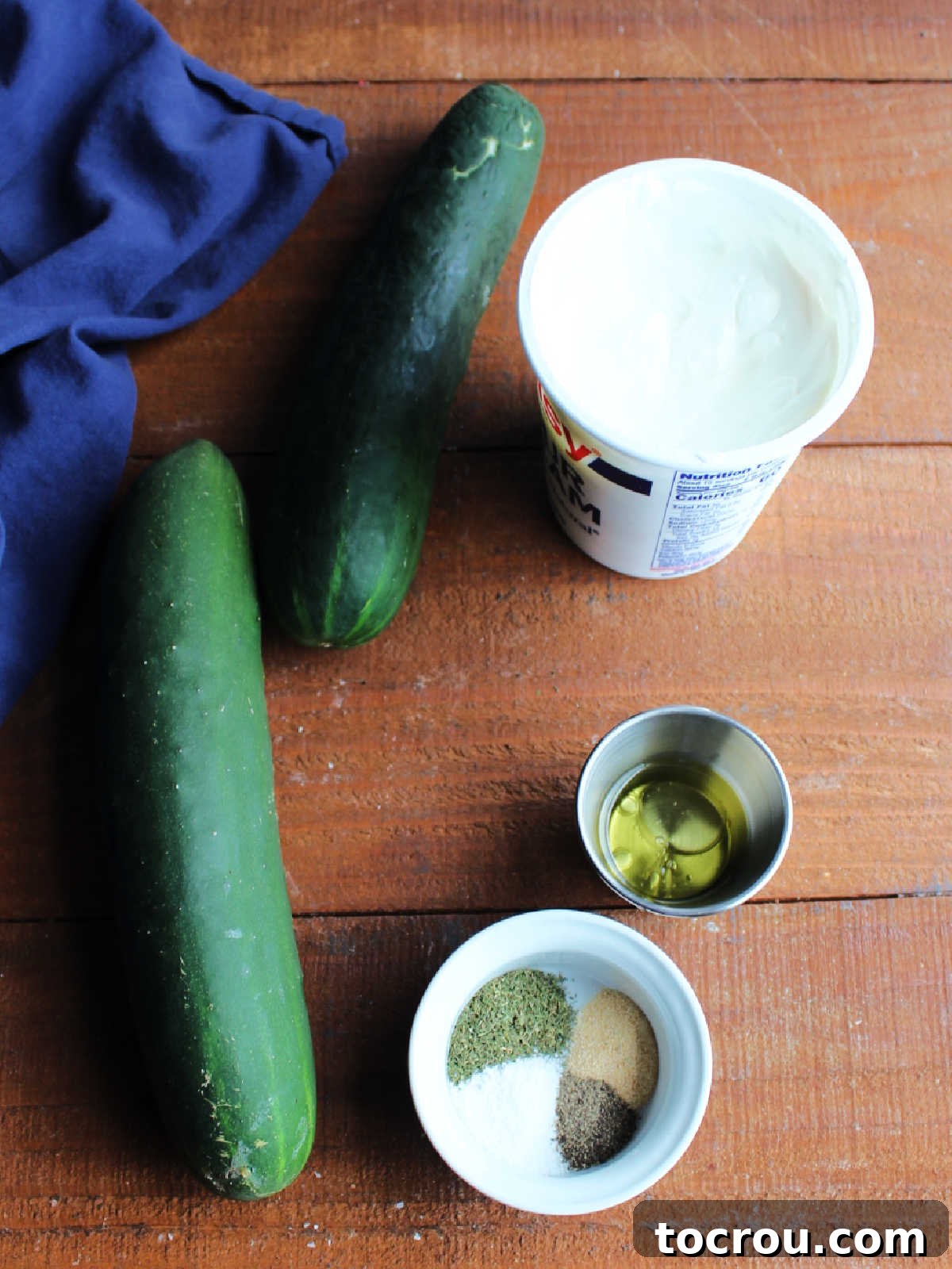 Ingredients including a couple of medium cucumbers, sour cream, vinegar, sugar, salt, dill, garlic, and pepper ready to be made into dilly cucumber salad.