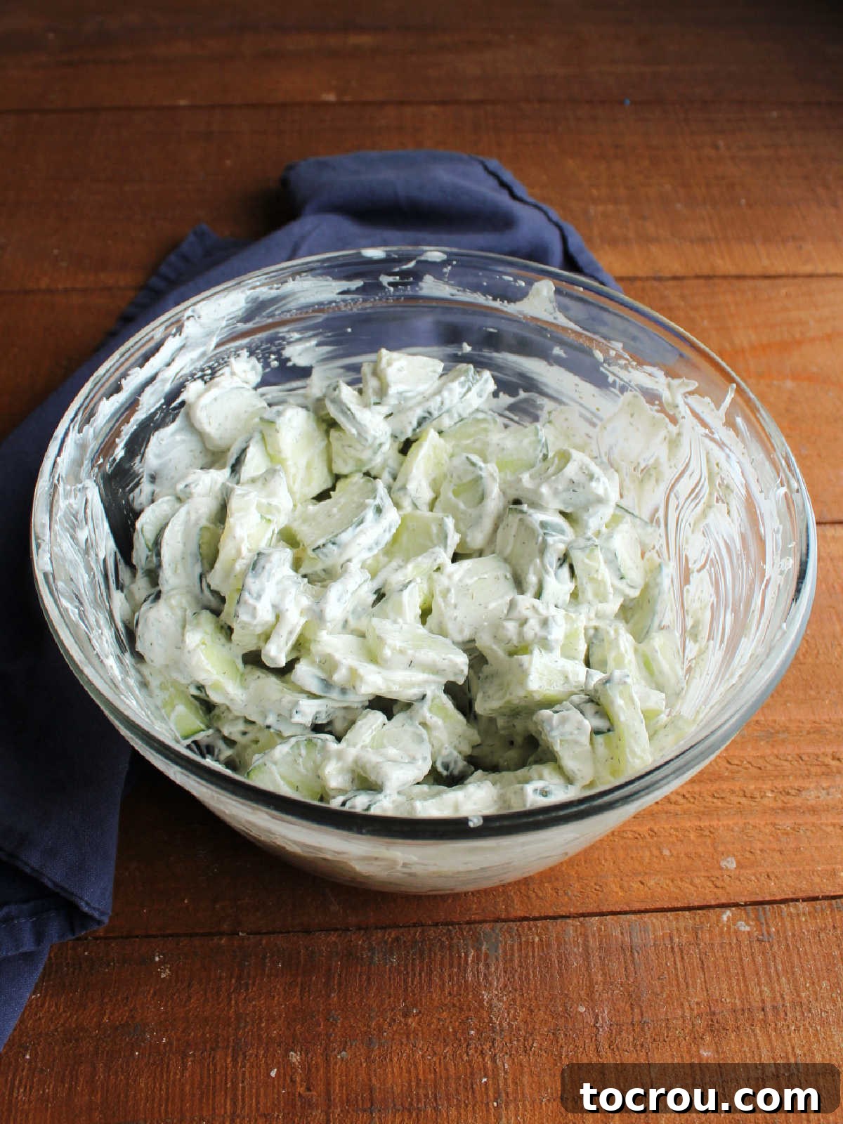 Mixing bowl filled with cucumber slices tossed in sour cream and dill dressing, ready to be chilled.