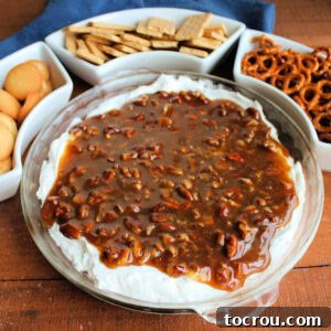 Pecan Pie Dip A pie plate brimming with decadent pecan pie dip, featuring a fluffy white cream cheese layer generously topped with a gooey brown sugar and pecan layer, accompanied by vanilla wafers, graham crackers, and pretzels for dipping.
