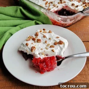 Frosted Cranberry Jello Salad A close-up view of a bite of frosted cranberry Jello salad, revealing the vibrant jello with suspended pineapple and a hint of coke, crowned with fluffy cream cheese frosting and crunchy pecans.