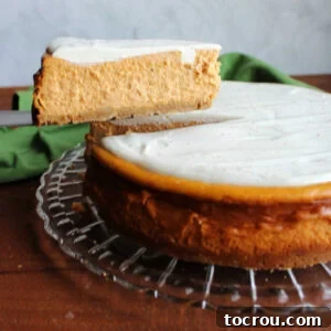 Easy Pumpkin Cheesecake A perfect slice of creamy pumpkin cheesecake with a dollop of white sour cream topping being lifted from the whole cake, showcasing its rich, autumnal hue and smooth texture.