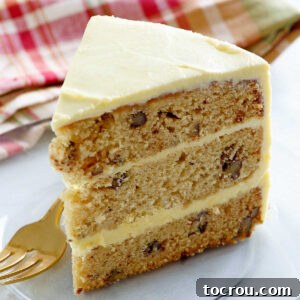 Maple Pecan Layer Cake A beautiful slice of maple pecan layer cake, showcasing three tender layers of tan cake studded with pecans, separated by a smooth and luscious maple buttercream frosting.