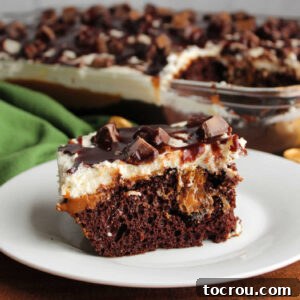 A delicious piece of Rolo poke cake, highlighting the chocolate cake base with tunnels of dulce de leche, topped with creamy ermine frosting, scattered Rolo candy bits, and a rich fudge sauce.