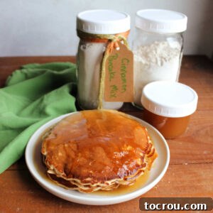 Plate of homemade cinnamon pancakes with apple cider syrup next to a couple of jars of homemade cinnamon pancake mix and a jar of homemade apple cider syrup.