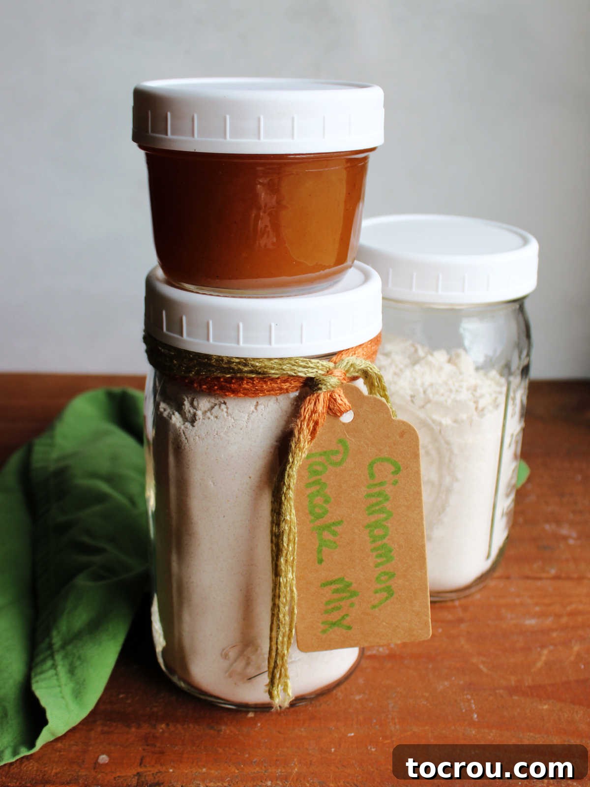 Jars of homemade cinnamon pancake mix along with a small jar of homemade apple cider syrup ready to be gifted. 