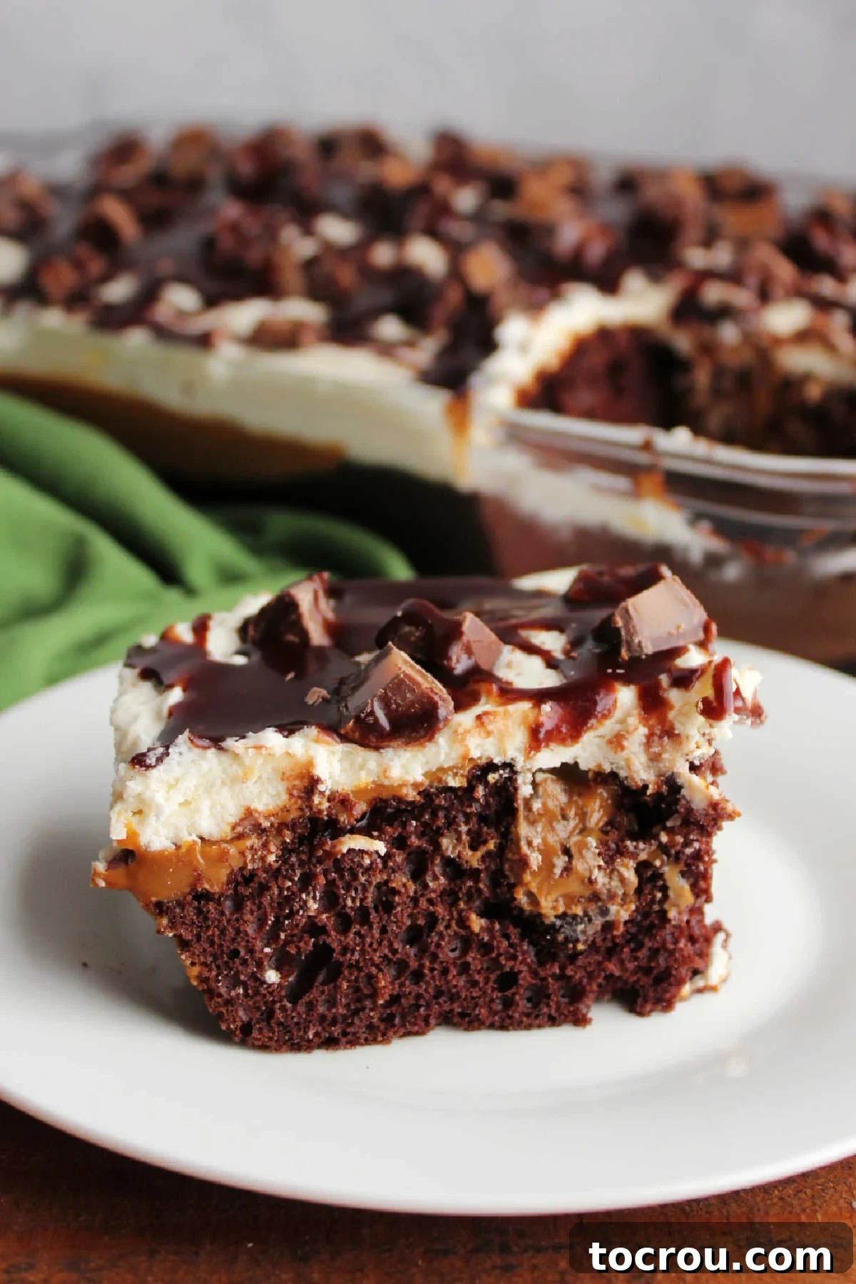 Slice of chocolate cake with caramel sauce coating, fluffy vanilla icing, hot fudge, and Rolo candy pieces.