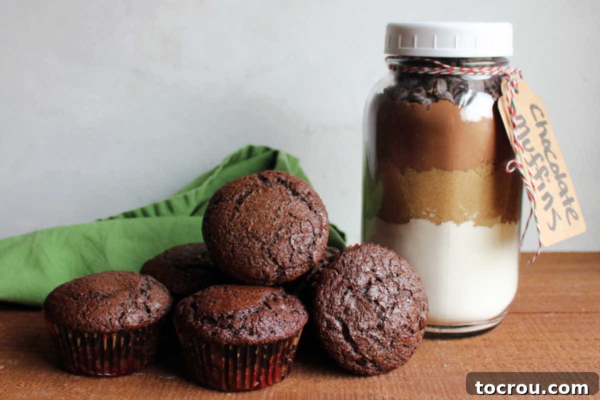 Jar of homemade double chocolate muffin mix next to a pile of rich chocolate muffins.