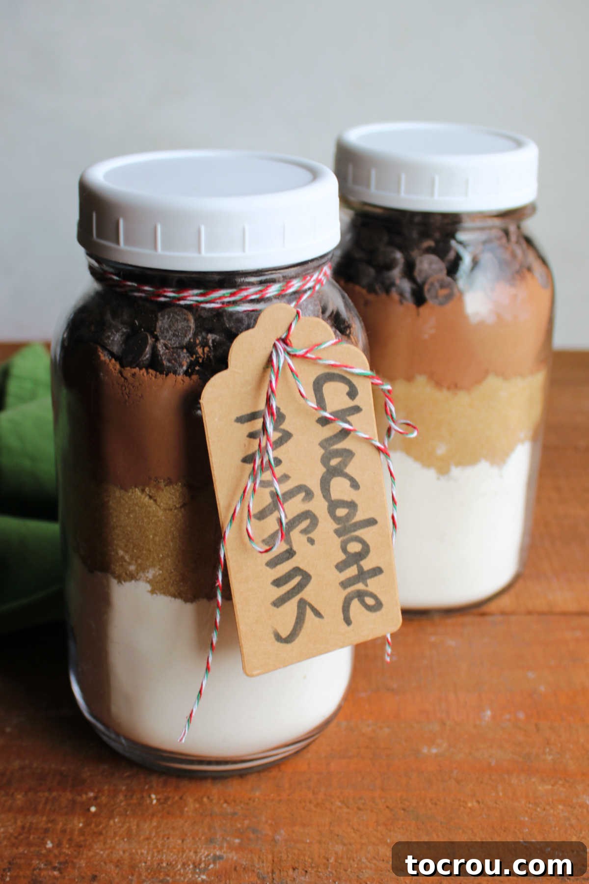 Two quart jars with layers of ingredients to make chocolate muffins inside and a tag tied to one with the baking instructions.