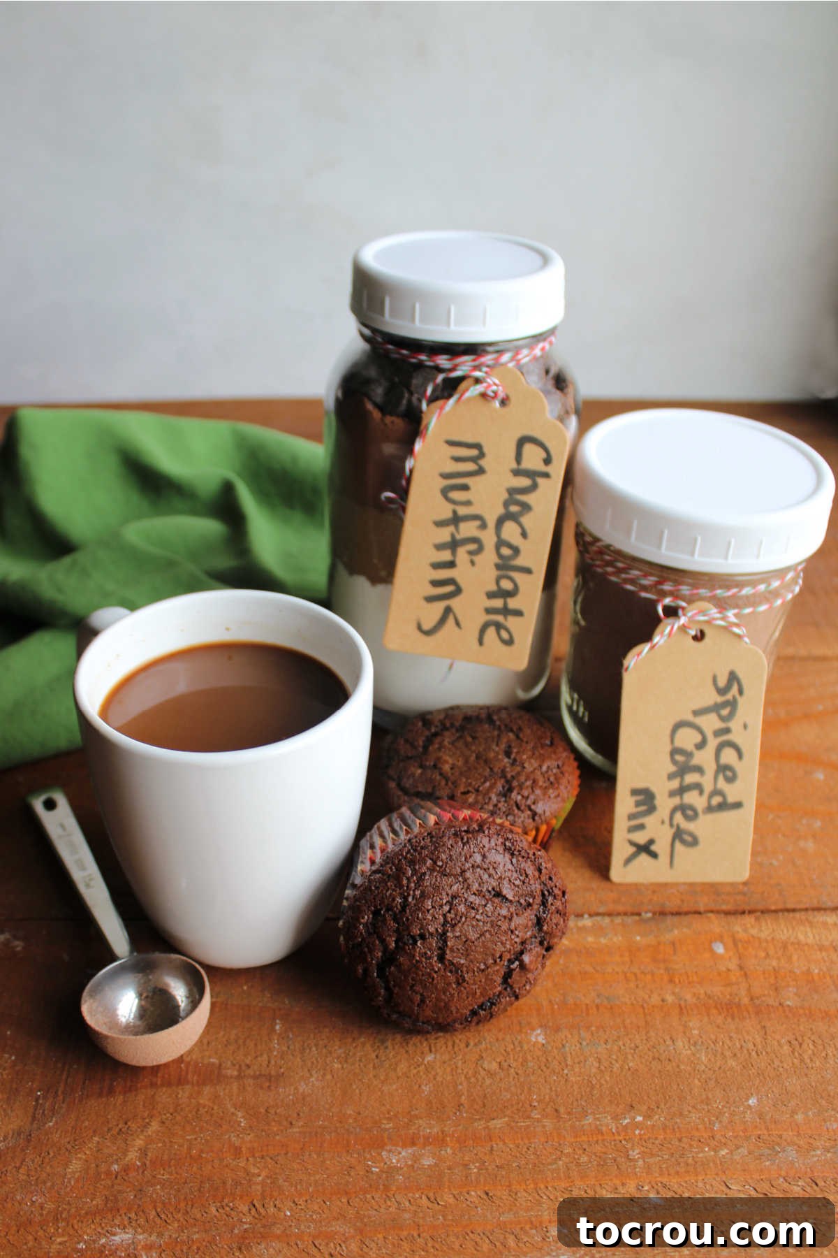 Homemade chocolate muffins next to a mug of spiced Christmas coffee along with jars containing the muffin mix and the coffee mix.
