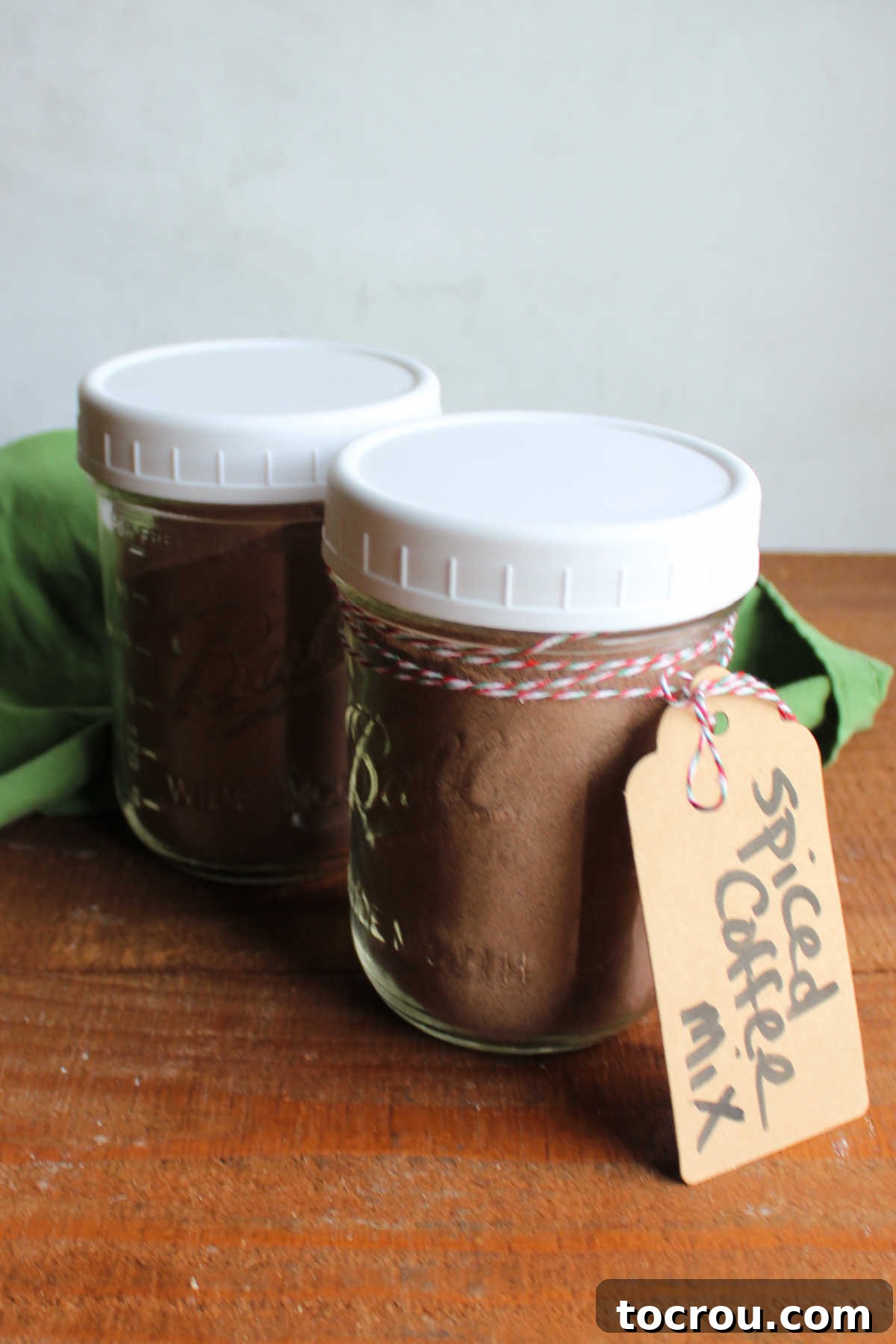 Two pint jars filled with spiced Christmas coffee powders with a tag saying what it is tied on it with festive bakers twine. 