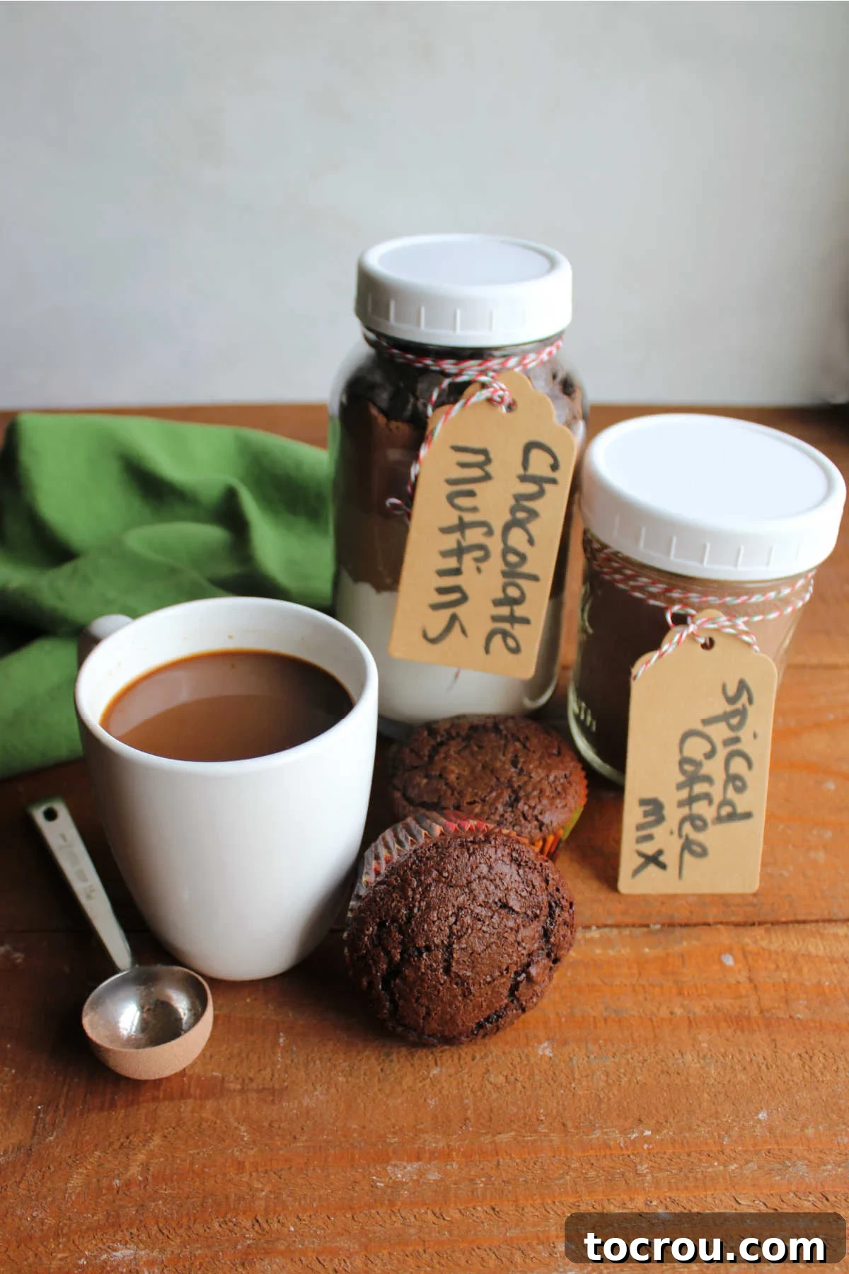 Homemade chocolate muffins next to a mug of spiced Christmas coffee along with jars containing the muffin mix and the coffee mix.