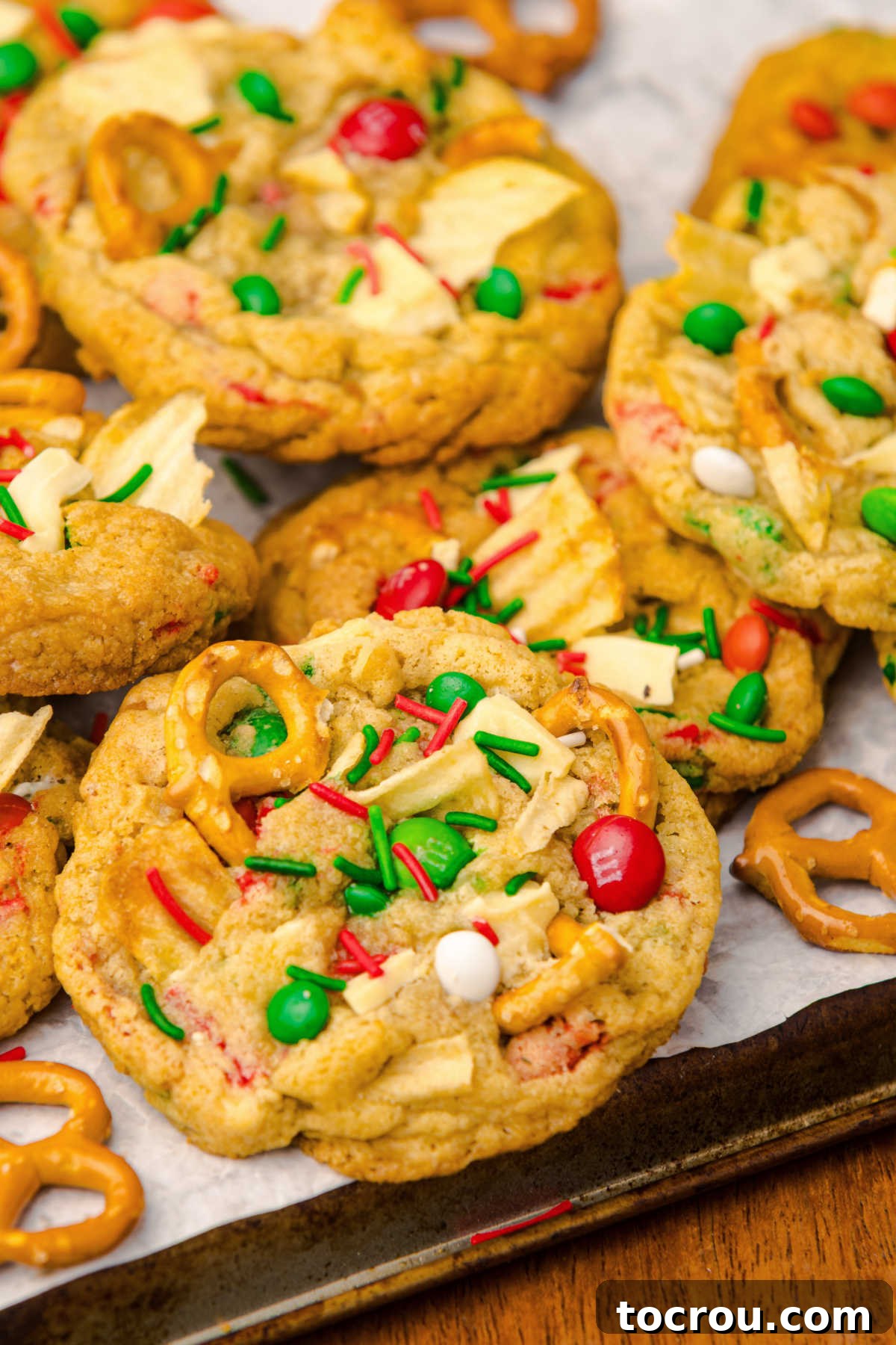 Tray of baked kitchen sink cookies filled with Christmas colored candies, sprinkles, pretzels, potato chips, and chocolate chunks, ready to eat. 